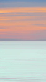 A tranquil ocean scene with soft pastel skies reflecting on calm water.
