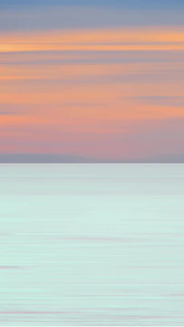 A tranquil ocean scene with soft pastel skies reflecting on calm water.