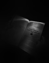 An open book held by someone's hands is illuminated by a focused light source in an otherwise dark environment. One page features a heading 'Creating Consistent Content That Readers Love' and some text below it.