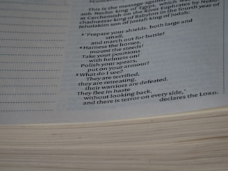 A close-up view of an open book showing a passage with text, which includes a poetic description of preparing for battle with commands and feelings of fear and retreat. The page is slightly curved, with visible lines and margins on the left side.