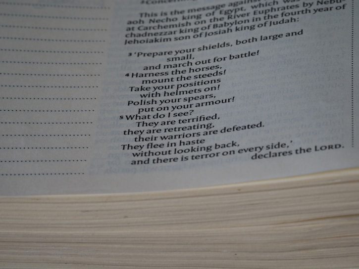A close-up view of an open book showing a passage with text, which includes a poetic description of preparing for battle with commands and feelings of fear and retreat. The page is slightly curved, with visible lines and margins on the left side.