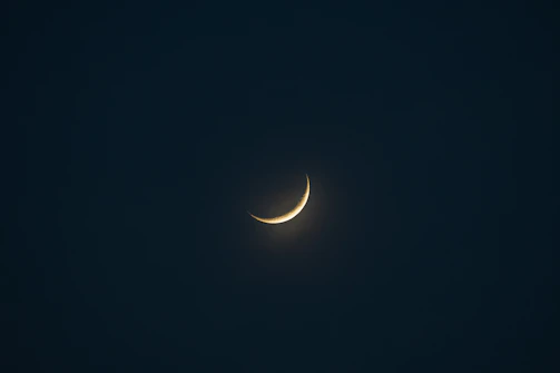A serene scene featuring a thin crescent moon symbol illuminated softly above a luxurious tarot reading setup.