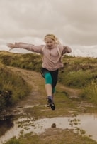 A joyful young girl jumping in colorful sneakers across a grassy park path.