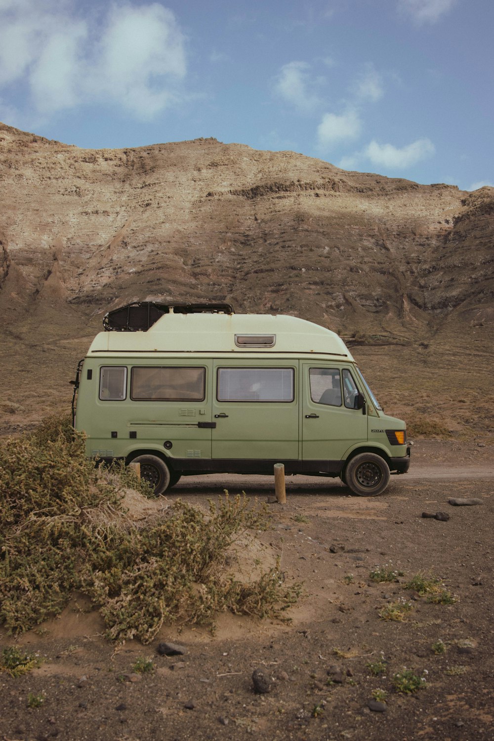 a green van parked on the side of a dirt road
