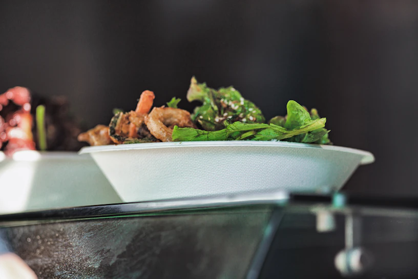 Close-up of a hand holding a biodegradable areca leaf plate with fresh salad, sunlight filtering through green leaves in the background.