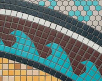 A geometric tile pattern featuring a combination of square and hexagonal tiles. The tiles are arranged in a wavy design with contrasting colors including brown, turquoise, black, white, and yellow. The hexagonal tiles are primarily at the top in blue and beige tones, while the square tiles below form a dynamic, undulating pattern.