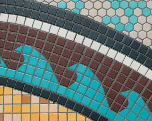 A geometric tile pattern featuring a combination of square and hexagonal tiles. The tiles are arranged in a wavy design with contrasting colors including brown, turquoise, black, white, and yellow. The hexagonal tiles are primarily at the top in blue and beige tones, while the square tiles below form a dynamic, undulating pattern.