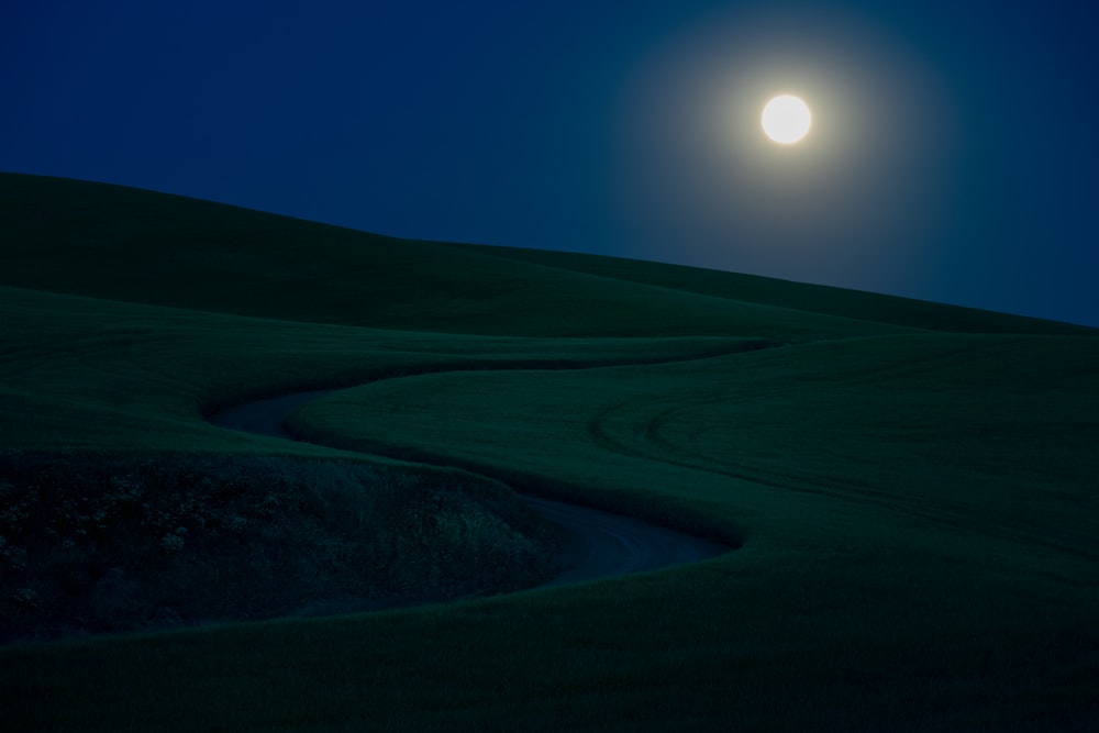 a full moon setting over a grassy hill