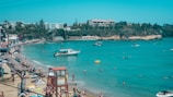 A lively beach scene with turquoise waters and sunbathers under umbrellas.