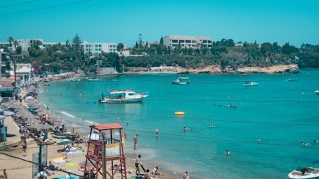 A lively beach scene with turquoise waters and sunbathers under umbrellas.