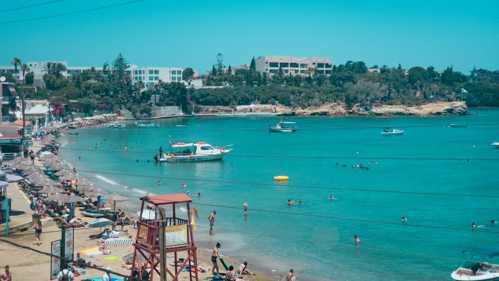 a crowded beach with boats and people in the water