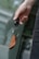 A hand holding a car key fob attached to a brown leather key holder in front of a blurred background.