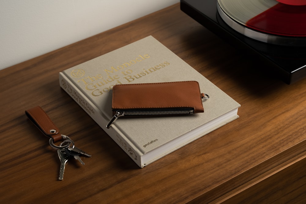 a brown wallet sitting on top of a book next to a pair of keys