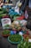 A vibrant market stall displays a variety of fresh produce. There are baskets filled with limes, pineapples, cucumbers, and other leafy greens. Plastic bags, crates, and sacks are scattered around, indicating an active trading area. Price tags are visible on some products.