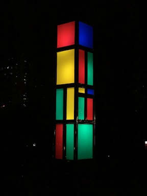 A tall rectangular column made up of illuminated panels in different colors including red, yellow, green, and blue, standing in a dark environment.