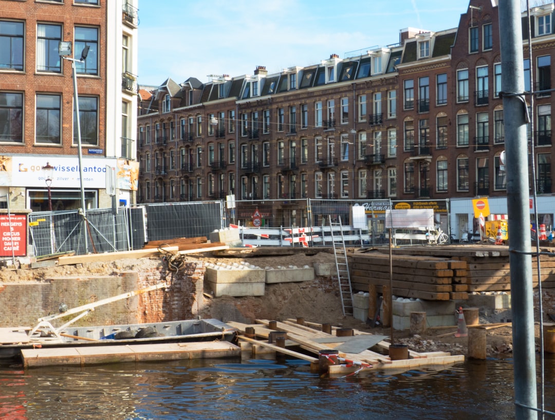 a construction site in the middle of a city, Construction works of the canal qays, because the original bridge here wil be rebuilt. Location is the crossing of the streets Ruysadaelkade and Ceintuurbaan in Amsterdam city. The old quays are rather fragile and must be reinforced first before they rebuilt the bridge to the richt side. Street photography of house facades in old city Amsterdam by Fons Heijnsbroek; free download urban photo, The Netherlands. This street image I share in suitable high resolution for making a nice art print or wallpaper.