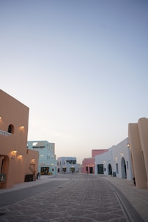 A quiet street lined with pastel-colored buildings under a pale blue sky.