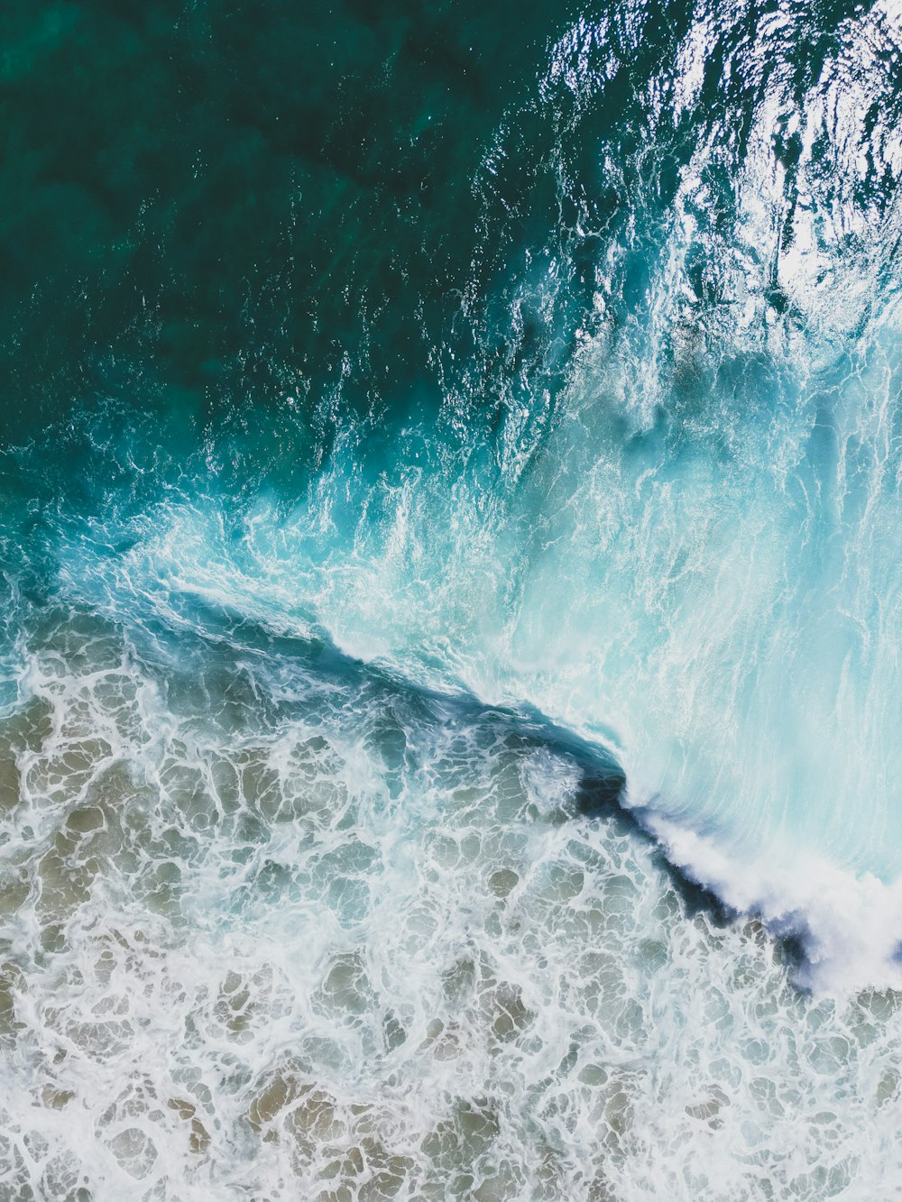 an aerial view of a wave breaking into the ocean