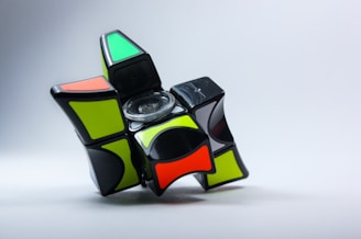 A partially disassembled or twisted 3x3 puzzle cube with colorful stickers, including green, orange, and black, against a simple gray background.
