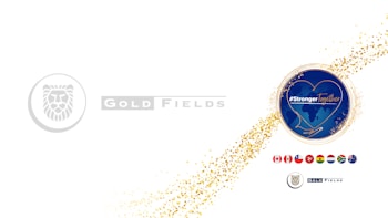 A white background with two main graphic elements. On the left, there is a logo of a stylized lion within a circle, accompanied by the text 'Gold Fields' in a grey font. On the right, a circular emblem with a blue background features a heart outline and the words '#StrongerTogether' overlaid on a map. A trail of gold confetti connects these elements, and below the emblem, several national flags are displayed in a row.