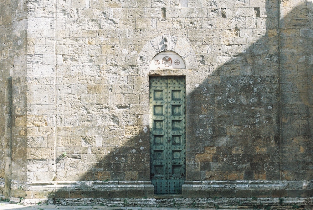 a tall green door sitting in the middle of a stone wall