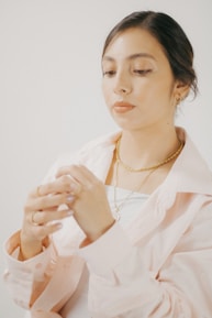 A stylish woman wearing a blush pink necklace, smiling softly in natural light.