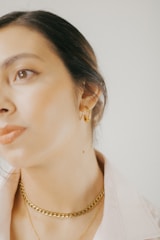 Close-up of a woman wearing a simple gold necklace and diamond studs, glowing softly in natural light.