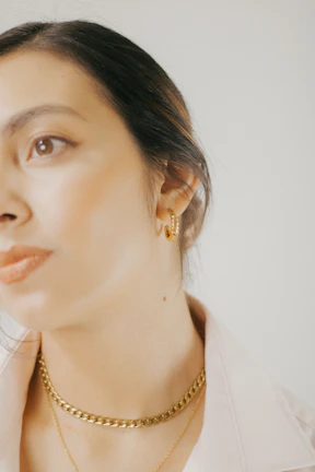 Close-up of a woman wearing elegant gold-plated earrings and a matching necklace in soft natural light.