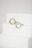 Two metal rings, one silver and one gold, are placed on a minimalist white staircase. The rings are modern and geometric in design, featuring round open shapes. The background is a plain, soft white, accentuating the elegance and simplicity of the objects.