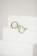 Two metal rings, one silver and one gold, are placed on a minimalist white staircase. The rings are modern and geometric in design, featuring round open shapes. The background is a plain, soft white, accentuating the elegance and simplicity of the objects.