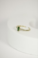 Macro shot of a custom emerald ring with delicate band details highlighted in soft champagne gold lighting.