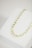 A delicate gold necklace with small, circular discs and beads is placed on a white jewelry display stand.