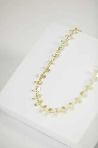 Delicate 18k gold necklaces with unique pendants displayed on a rustic wooden table.