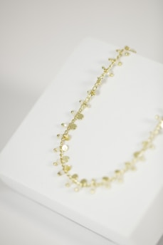 A delicate gold necklace with small, circular discs and beads is placed on a white jewelry display stand.