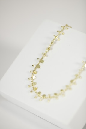 A delicate gold necklace with small, circular discs and beads is placed on a white jewelry display stand.