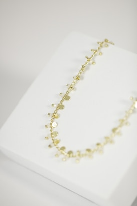 A delicate gold necklace with small, circular discs and beads is placed on a white jewelry display stand.