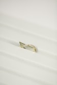 A gold ring with a twisted design, encrusted with small diamonds, placed on a white textured surface.