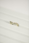 A gold ring with a twisted design, encrusted with small diamonds, placed on a white textured surface.