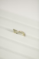 A gold ring with a twisted design, encrusted with small diamonds, placed on a white textured surface.