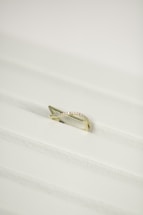 A gold ring with a twisted design, encrusted with small diamonds, placed on a white textured surface.