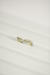 A gold ring with a twisted design, encrusted with small diamonds, placed on a white textured surface.