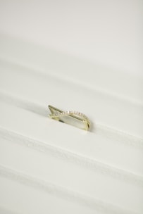 A gold ring with a twisted design, encrusted with small diamonds, placed on a white textured surface.