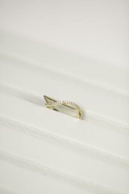 A gold ring with a twisted design, encrusted with small diamonds, placed on a white textured surface.