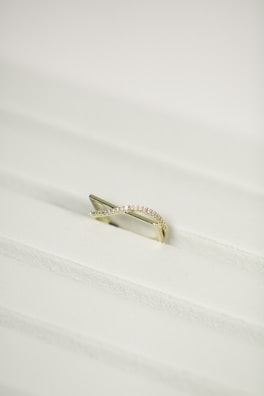 A gold ring with a twisted design, encrusted with small diamonds, placed on a white textured surface.