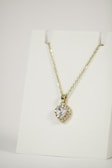 A gold necklace is adorned with a heart-shaped pendant featuring a central clear gemstone surrounded by smaller stones. The necklace is displayed on a plain white background, emphasizing its elegant design.