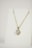 A gold necklace is adorned with a heart-shaped pendant featuring a central clear gemstone surrounded by smaller stones. The necklace is displayed on a plain white background, emphasizing its elegant design.