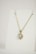 A gold necklace is adorned with a heart-shaped pendant featuring a central clear gemstone surrounded by smaller stones. The necklace is displayed on a plain white background, emphasizing its elegant design.