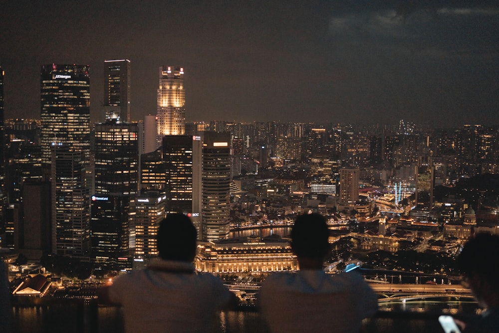two people sitting on a ledge overlooking a city at night