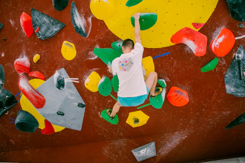A bouldering athlete mid-move on an indoor wall, fingers taped with climbingtape for support and protection.