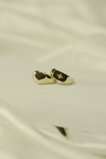 A pair of gold-toned cufflinks with a black enamel section featuring a small engraved star design placed elegantly on a soft, cream-colored fabric background.